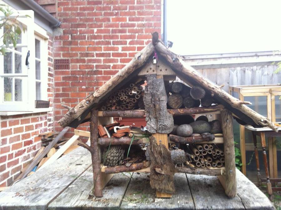 A large rustic bug hotel filled with logs, canes and cones